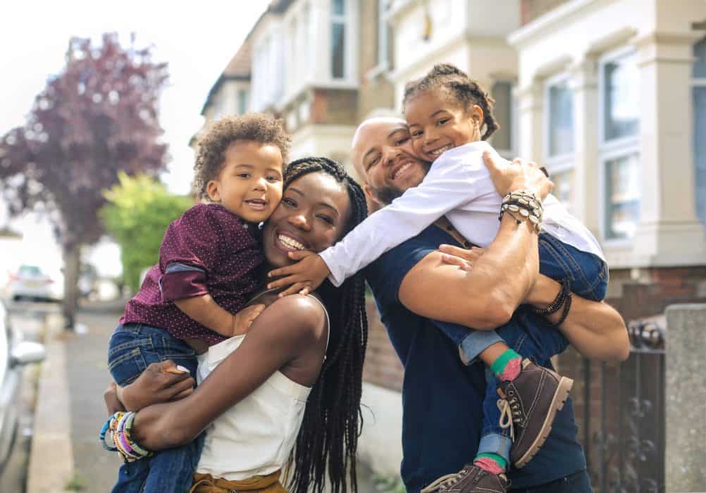 Family of four stands in front of home on tree-lined street