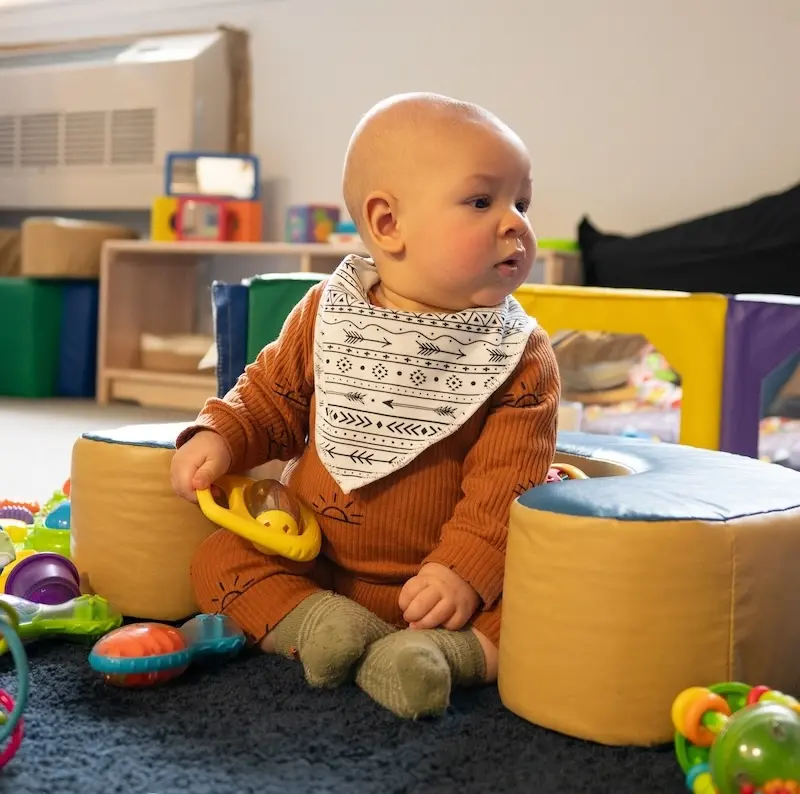 A young girl sitting at a table playing with Play-Doh in a colorful preschool classroom.