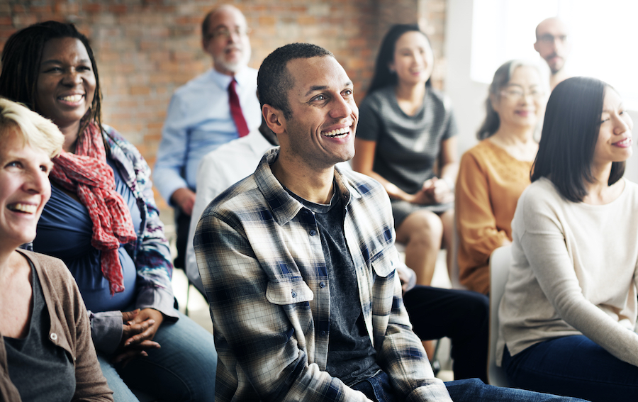 A cheerful and diverse group of people sitting in the audience of a presentation.