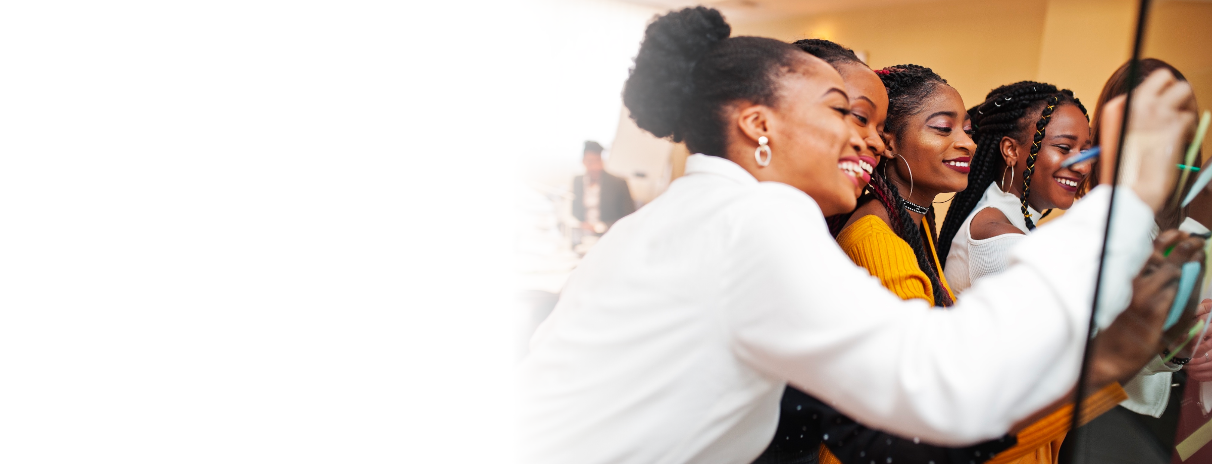 Four black women smiling and drawing together on a dry-erase board just out of the image frame.