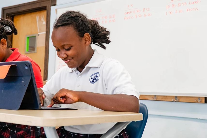 A young black girl smiling at her desk as she works on her computer.