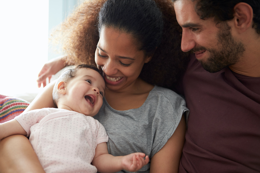 A young happy couple cradling their baby together. The baby is smiling back at their parents.