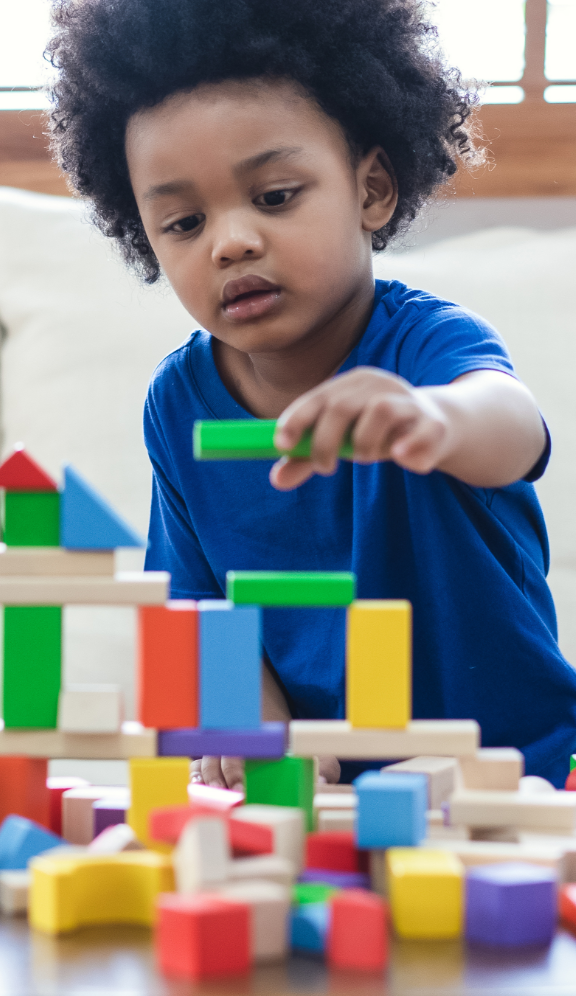 Young boy placing a toy block on top of a toy block structure