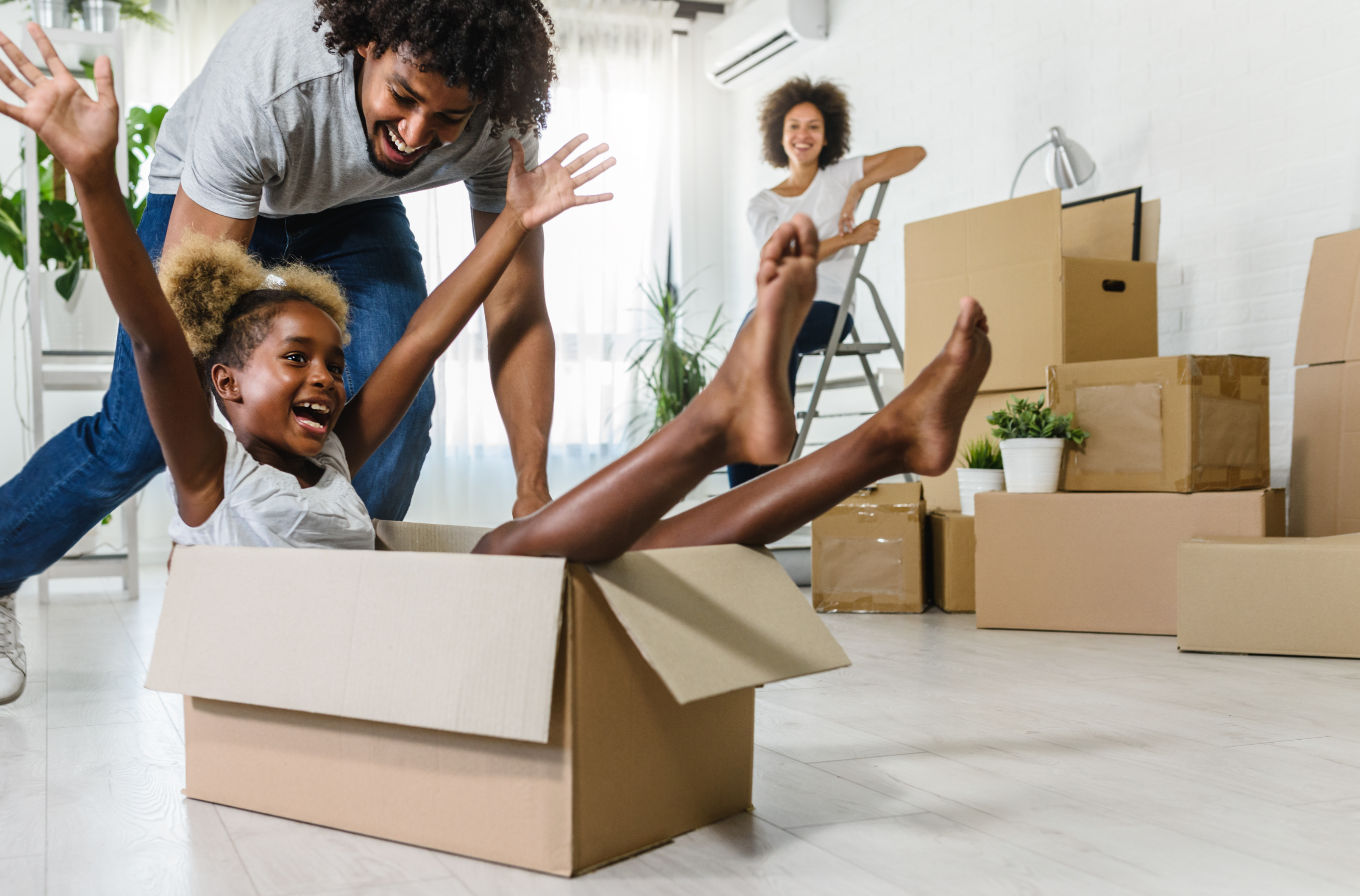 Young girl playing in packing box with her mother and father smiling behind her