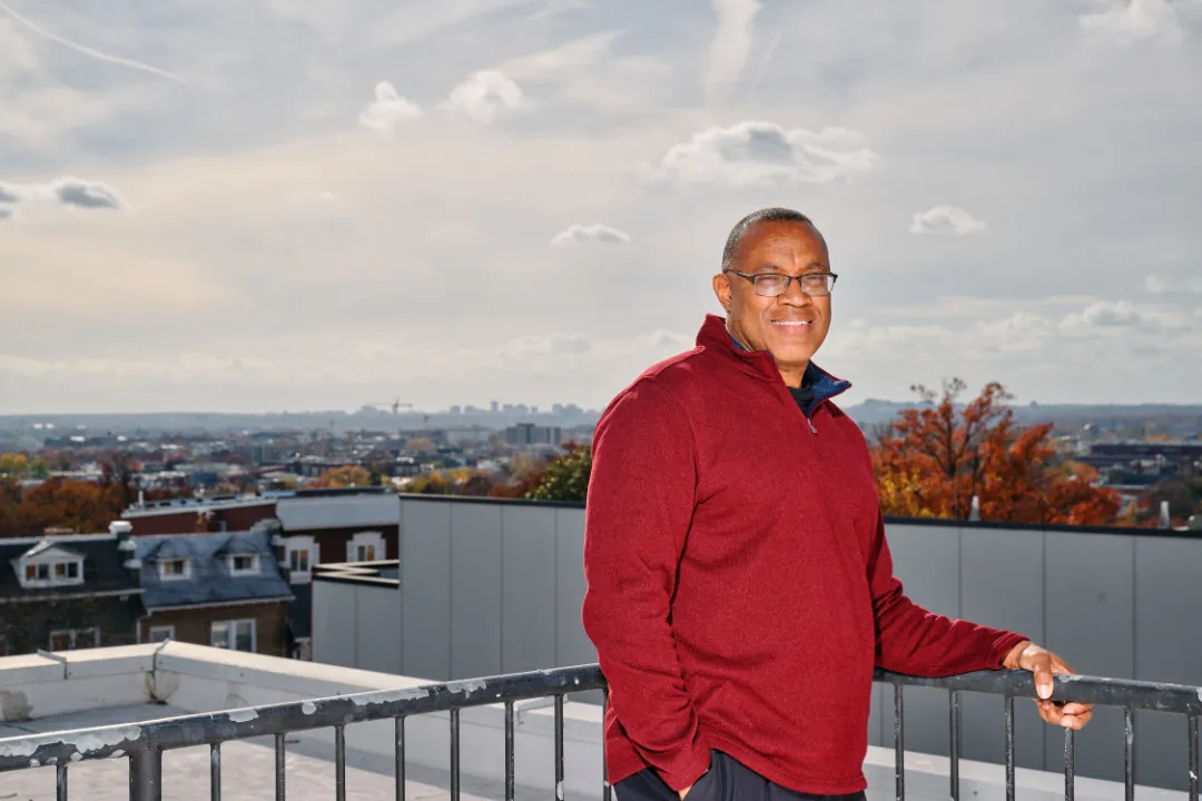 Portrait of a person on a building rooftop with houses and sky in the background.