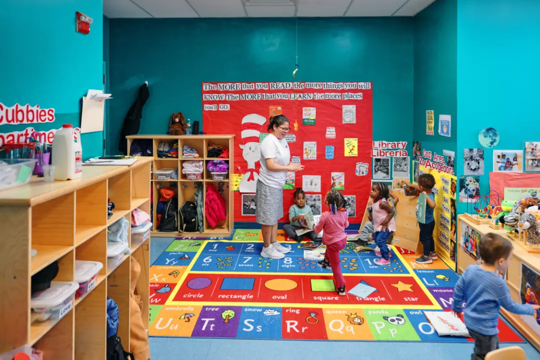 Photo of a school classroom with an adult and five small children.