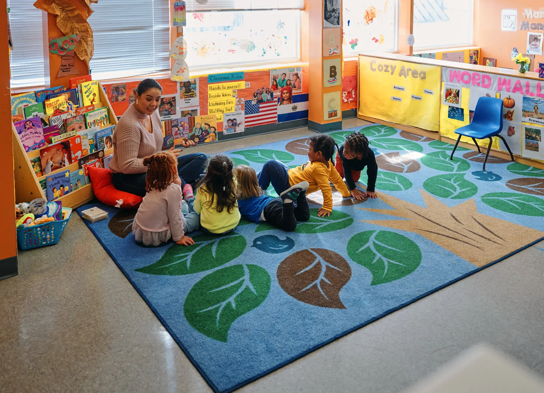 Five children sitting on a carpet listening while an adult talks to them.
