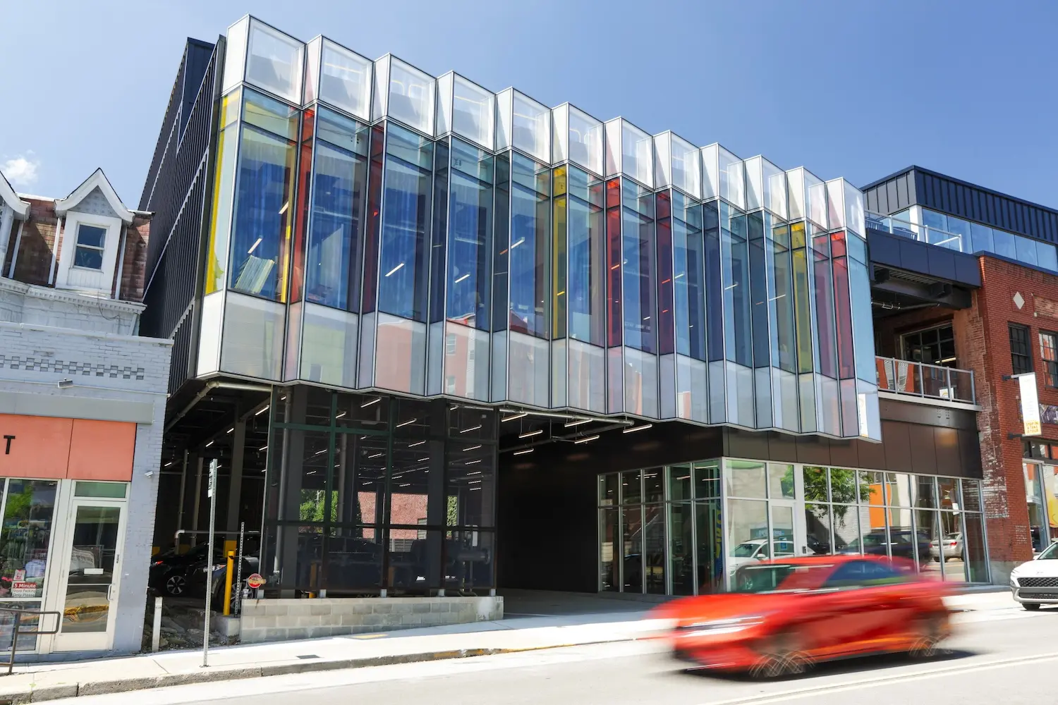 A car passes by a vibrant building featuring a strikingly colorful glass facade.