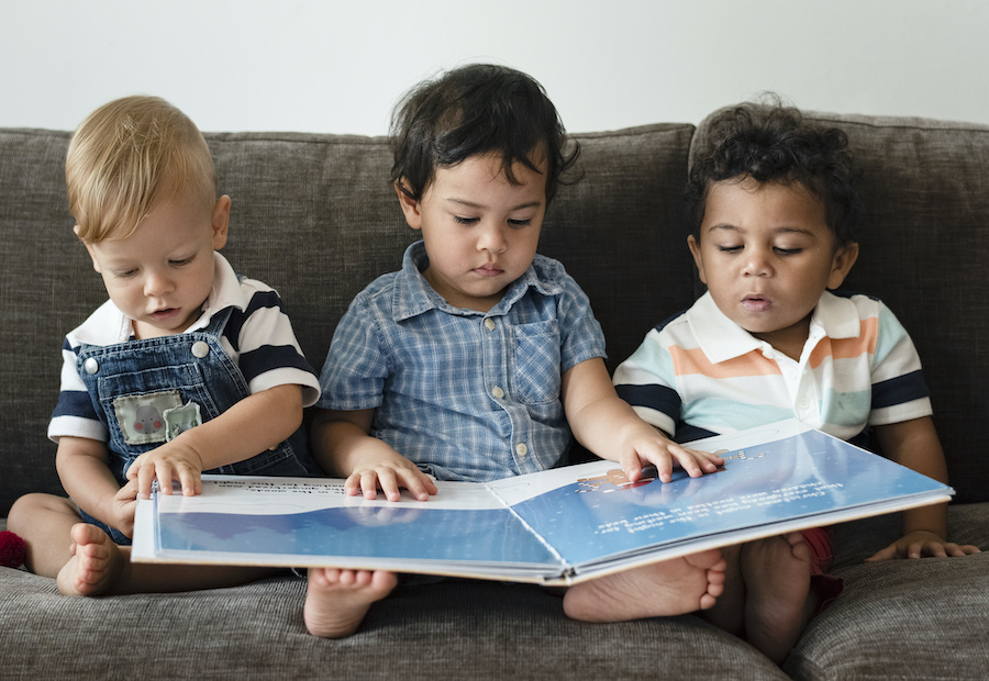 Three kids sitting and reading a large book together.